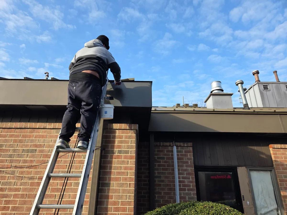 Técnico pintando moldura metálica de un edificio comercial de ladrillo en una escalera